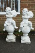 A pair of painted garden statues in the form of putti atop balls, 40" high