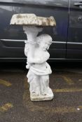 A painted concrete adapted birdbath in the form of a cherub holding a cornucopia with a clam shell