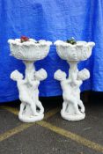 A pair of painted concrete raised garden planters, the planters held aloft by two cherubs, 36" high,