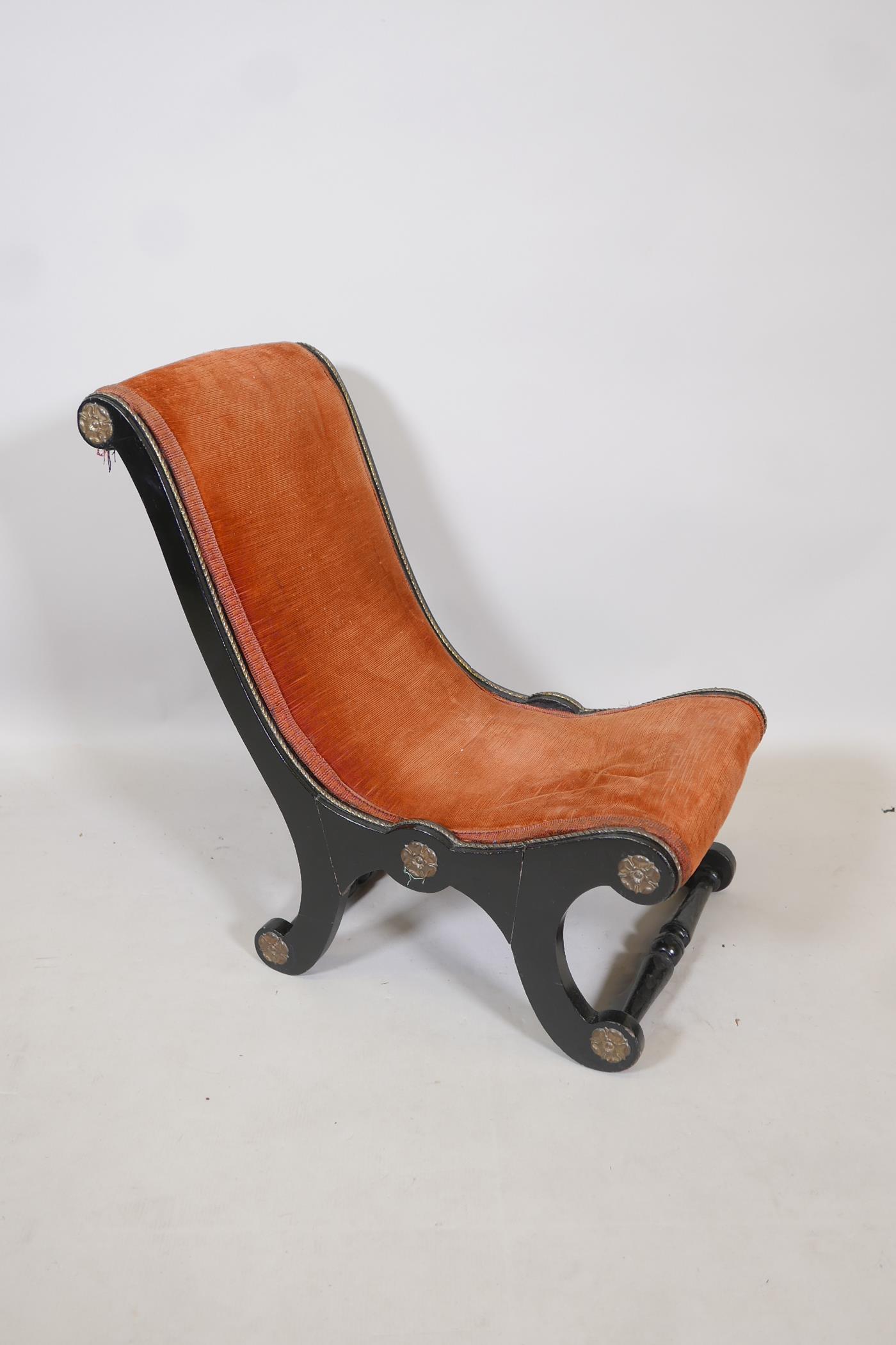 A Victorian ebonised slipper chair, with rust red upholstery and brass decorative motifs and trim,