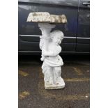 A painted concrete adapted birdbath in the form of a cherub holding a cornucopia with a clam shell