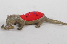 A brass pincushion cast as an otter with fish in its mouth, the otter textured with a hair effect