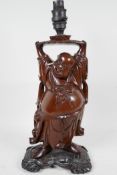 An Oriental hardwood lamp base carved as Hotai holding a lotus above his head which supports the