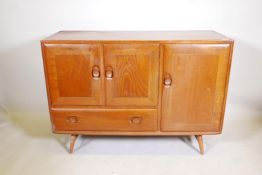 A mid C20th Ercol elm sideboard, with three cupboard doors and a single drawer, raised on turned