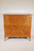 A C20th walnut veneered cocktail cabinet with cantilever front revealing a mirrored interior, over