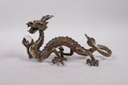 A Chinese bronze five toed dragon clutching a glass ball, 8" long