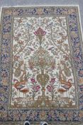 A Persian beige ground wool rug with a mirrored design of birds, trees and floral arrangements,