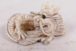 A bone netsuke carved as a coiled dragon with jet eyes, 1¾" long