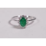 An 18ct white gold ring set with an oval emerald encircled by diamonds, approximately 60 points,