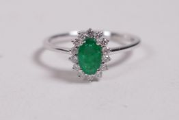 An 18ct white gold ring set with an oval emerald encircled by diamonds, approximately 60 points,