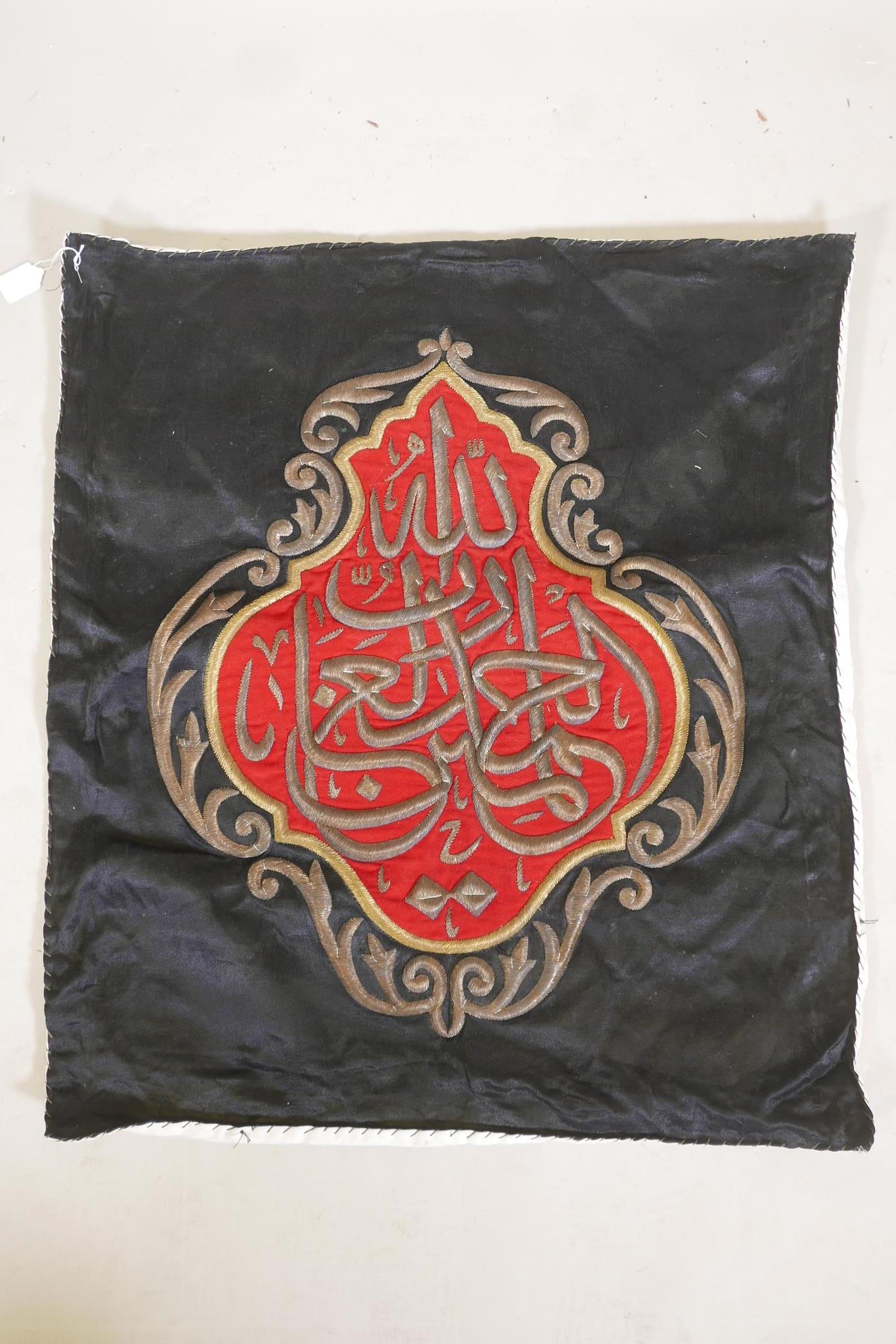 An Islamic wall hanging embroidered with calligraphy in gilt metal wire on a red ground, 32" x 27"