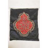 An Islamic wall hanging embroidered with calligraphy in gilt metal wire on a red ground, 32" x 27"