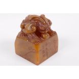A Chinese square section carved soapstone seal, the top carved as a mythical beast, signed to the