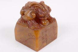 A Chinese square section carved soapstone seal, the top carved as a mythical beast, signed to the