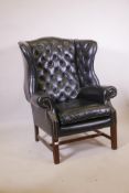 A Georgian style wing back armchair with button back leather upholstery and brass studs, raised on