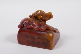A Chinese mottled amber and red soapstone seal with carved decoration of a toad on a lily pad,