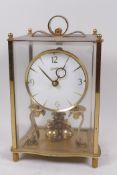 A brass cased silk suspension mantel clock by Kundo, in a four glass case, 9" high