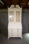 A painted fall front bureau bookcase in two sections, the upper with carved and pierced swan neck