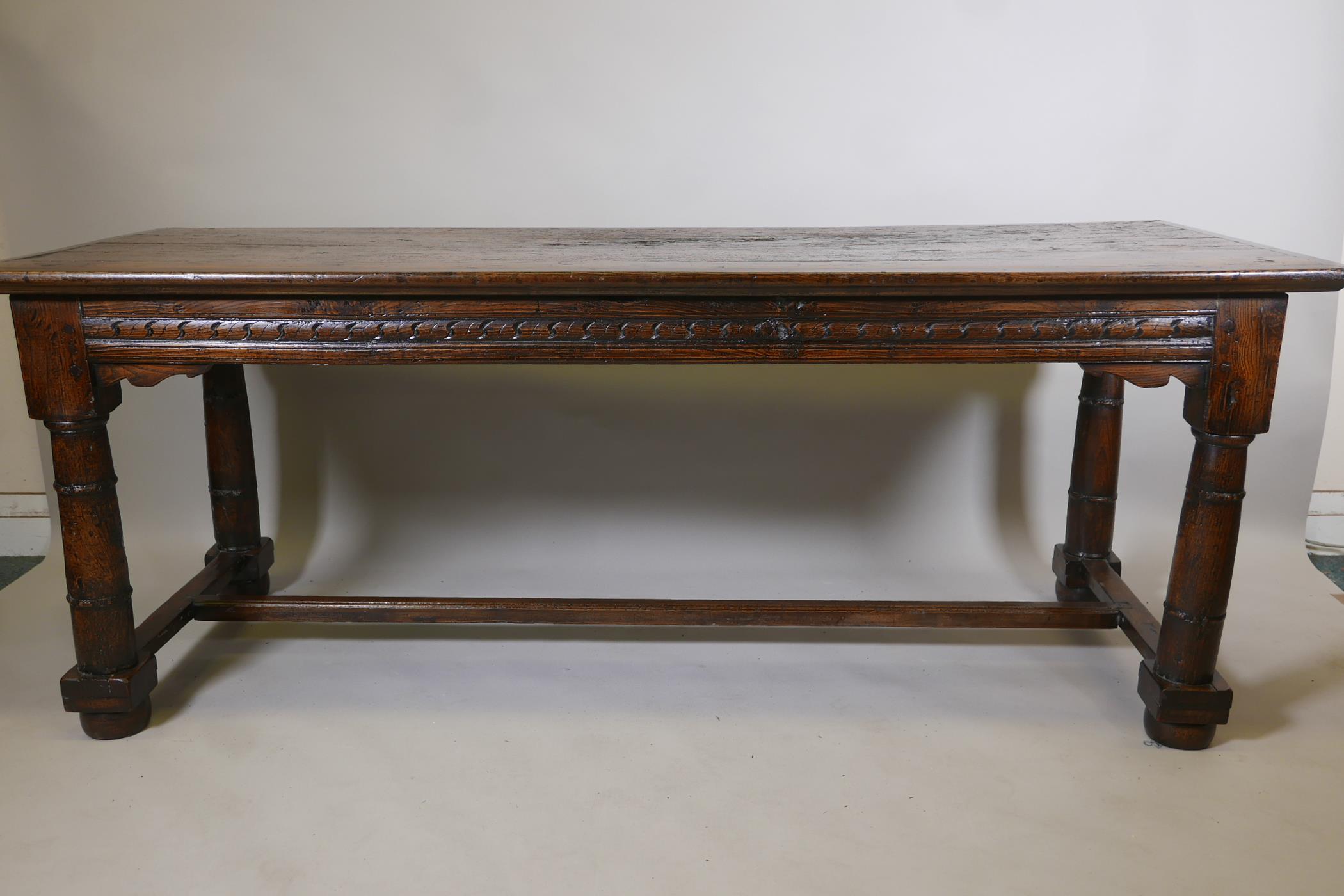 An antique oak refectory table, with plank top and carved frieze raised on gun barrel turned