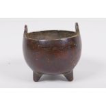 A miniature Chinese bronze cauldron shaped censer with two loop handles and three cast feet,