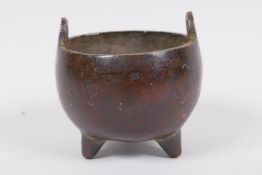 A miniature Chinese bronze cauldron shaped censer with two loop handles and three cast feet,