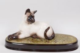 A Beswick figure of a Siamese cat, on a grassy plinth, 11½" long