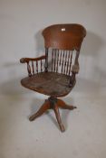 An American oak tilt and swivel desk chair with spindle back, stamped Angus, London, Manufactured in