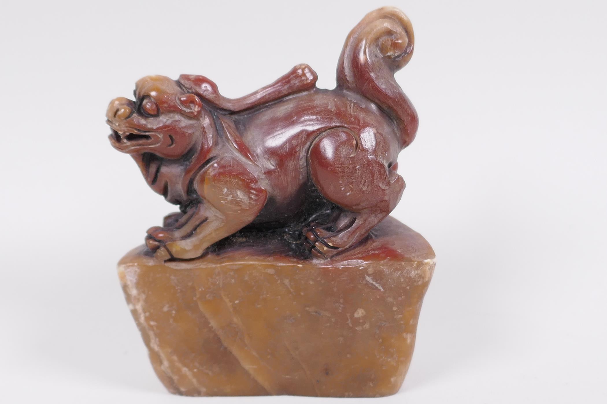 A Chinese carved soapstone seal, the top carved as a kylin on a shaped rock, 3" high