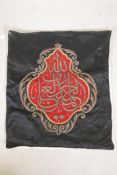 An Islamic wall hanging embroidered with calligraphy in gilt metal wire on a red ground, 32" x 27"