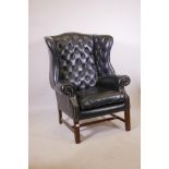 A Georgian style wing back armchair with button back leather upholstery and brass studs, raised on