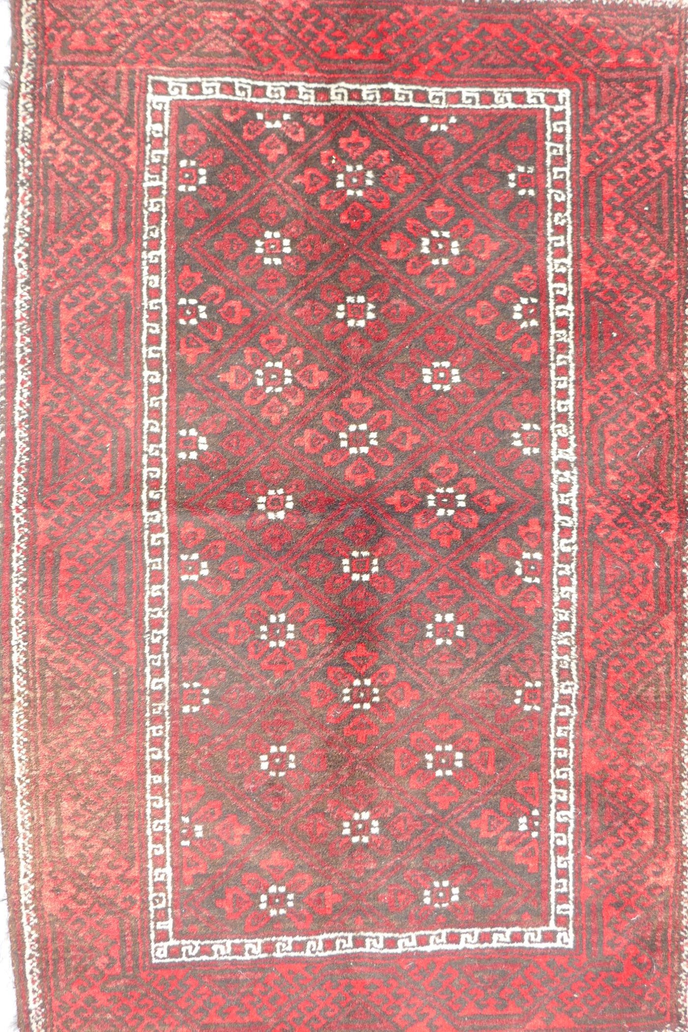 A Middle Eastern red ground wool rug with a repeating diamond pattern design, 34" x 51"