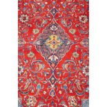A full pile fine woven Sarouk carpet with a floral medallion design on a red field, 112" x 78"