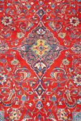 A full pile fine woven Sarouk carpet with a floral medallion design on a red field, 112" x 78"