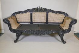 An Anglo Indian style settee with painted and carved wood frame, scroll arms and caned sides and