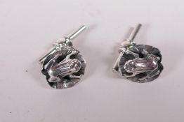 A pair of white metal cufflinks in the form of frogs on lily pads,