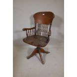 An American oak tilt and swivel desk chair with spindle back, stamped Angus, London, Manufactured in