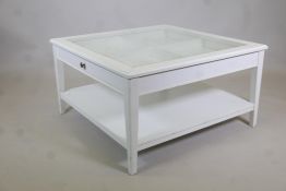 A painted coffee table with push-pull drawer and glass top, raised on tapering supports united by an