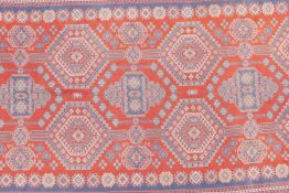 An oriental tomato ground woven rug decorated with a blue bokhara style design, 51" x 113"