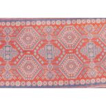 An oriental tomato ground woven rug decorated with a blue bokhara style design, 51" x 113"