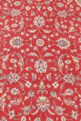 A French Persian style red ground wool carpet with scrolling floral decoration and ivory borders,