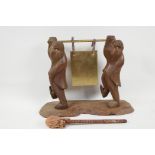 An oriental carved wood table gong supported by two dressed monkeys, 11" high, 15" wide