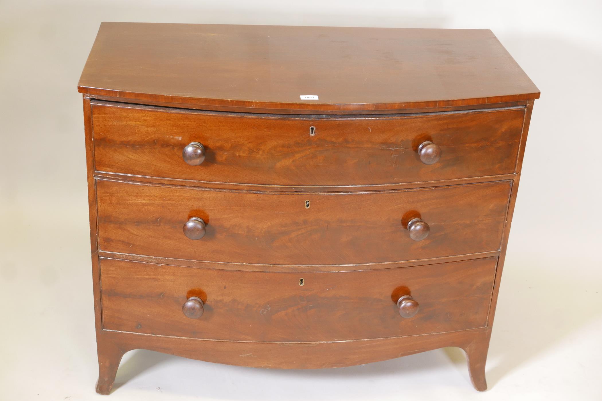 A George III mahogany bow fronted chest of three long drawers, with turned wood handles, raised on
