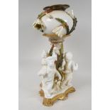 A C19th porcelain oil lamp base supported by three cherubs, the bowl encrusted with flowers in the