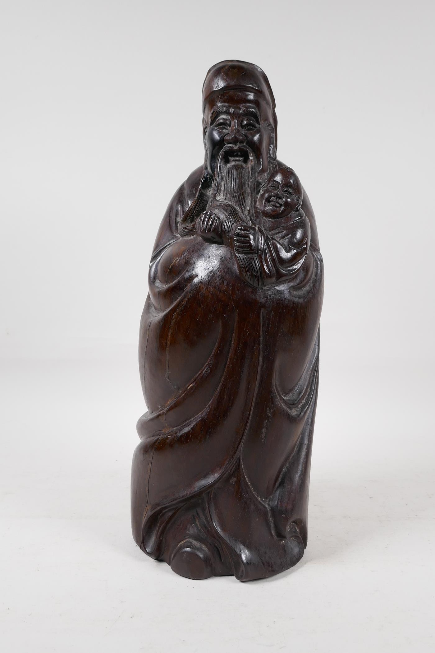 A Chinese carved hardwood figure of a sage carrying a child, 15" high
