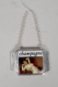 A silver plated and enamel champagne label decorated with a semi-clad woman, 3" x 2"