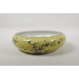 A Chinese yellow glazed porcelain bowl with a rolled rim and black and white floral decoration, seal