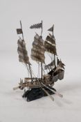 A white metal model of a Chinese junk, on a hardwood stand three oars missing, 7" high