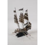 A white metal model of a Chinese junk, on a hardwood stand three oars missing, 7" high