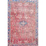 A Persian hand woven full pile rug with an all over floral design on a red field, with blue