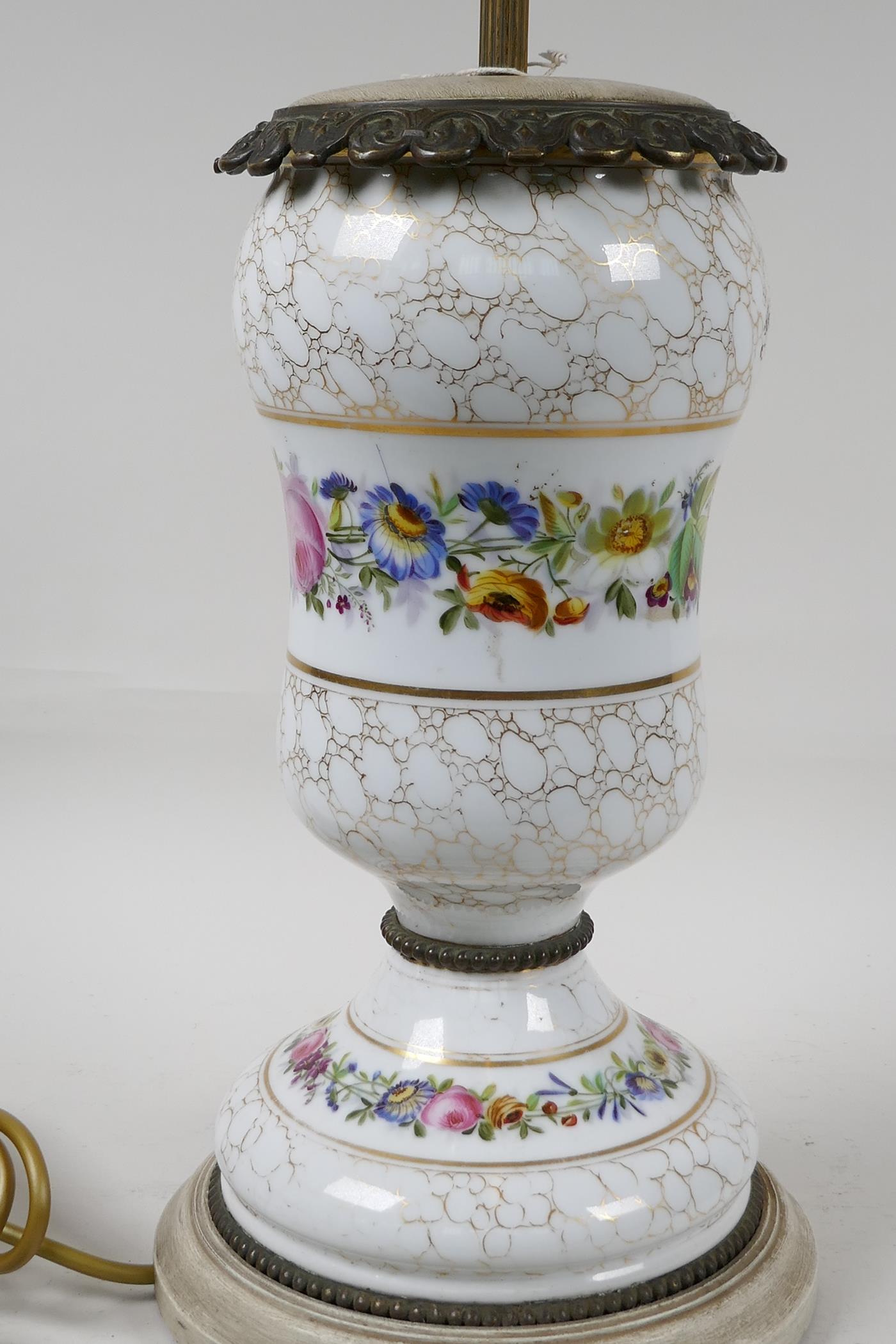 An urn shaped porcelain table lamp with ormolu mounts and painted with garlands of flowers, on a